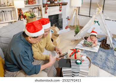 Asian family enjoying a cozy Christmas day at home. Elderly man and middle-aged woman sitting on couch, looking at a tablet, while their young boy, in a Santa hat, lounges nearby with Christmas gift. - Powered by Shutterstock