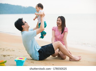 Asian Family Enjoying Quality Time On The Beach With Father, Mother And Daughter