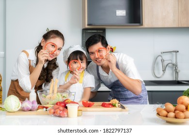 Asian Family With Father, Mother And Cute Little Girl Daughter  In Chef's Hats Are Having Fun While Cooking In Kitchen At Home