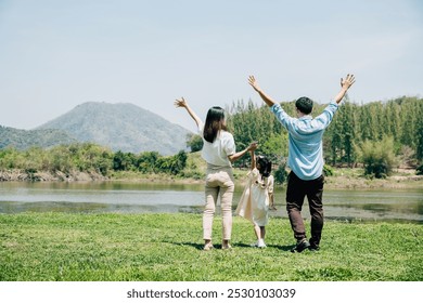 Asian family father mother and daughter stand front lake with raised hands sunny day in park, lifestyle parents and child kid enjoying outdoors together in nature on summer travel, Family relaxation - Powered by Shutterstock