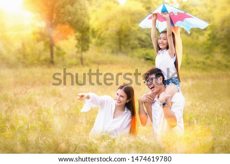 Asian family father, mother and daughter play ta kite in the outdoor park with sunrise and goldent colour, this image can use for family, relax, freedon, summer and travel concept