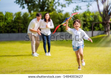 Asian family father, mother and daughter play a kite in the outdoor park in village near thay home, this image can use for family, relax, freedon, summer and travel concept