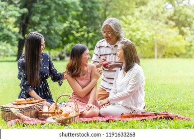 Asian Family Father's Mother And Beautiful Daughter, Sitting Picnic Enjoying A Holiday In Nature, Happily In The Park.