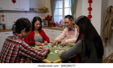 asian family of four shuffling tiles while playing  together on chinese new year's eve at home. chinese word at background translation: luck