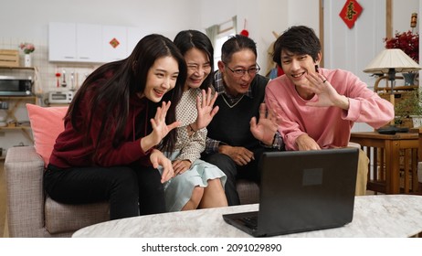 asian family of four waving hi and wishing friend happy chinese lunar new year with congratulation hand gestures through video chat on computer in the living room. text on door translation: spring