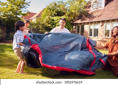 Asian Family In Garden At Home Putting Up Tent For Camping Trip Together