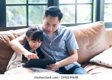 Asian Family Girl Kid And Father Using Tablet Playing Internet Online Together In Living Room At Home With Happiness And Smile. Two Gap Generation Of Technology And Education Usage Lifestyle Concept.