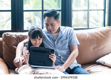 Asian Family Girl Kid And Father Using Tablet Playing Internet Online Together In Living Room At Home With Happiness And Smile. Two Gap Generation Of Technology And Education Usage Lifestyle Concept.