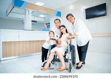 Asian family with grandmother, pregnancy woman, man and daughter stay in front of registration counter in hospital and they look at camera with happiness. - Powered by Shutterstock