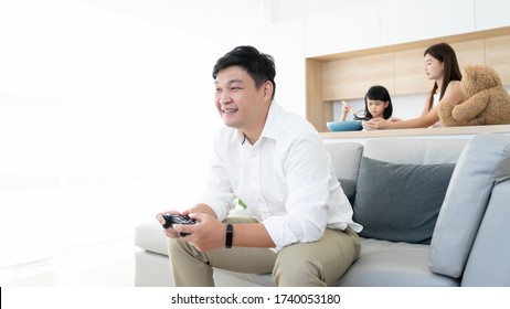 Asian Family Happy Resting Time In Long Weekend, Father Enjoy Play Console  Game Alone With Wife And Kids Learning Cooking In Kitchen Room Background With Copy Space