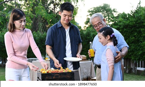 Asian Family Having A Barbecue Party At Home. Cooking Grilled Bbq For Dinner In Backyard. Lifestyle On Summer Holiday.