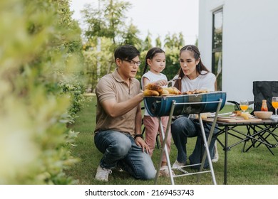 Asian Family Having Dinner In The Backyard At Home. Happy Family With Little Child Camping And Have Fun In House Backyard Outside. Barbecue Time, Family Activities Conccept.