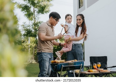 Asian Family Having Dinner In The Backyard At Home. Happy Family With Little Child Camping And Have Fun In House Backyard Outside. Barbecue Time, Family Activities Conccept.