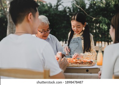 Asian Family Having Pizza In Garden At Home. Parent With Kid And Grandfather Lifestyle In Backyard.