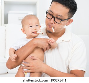 Asian Family At Home. Bad Father Smoking With Baby Together. Cigarette With Lit And Smoke. Unhealthy Lifestyle Or Stop Smoking Concept Photo.