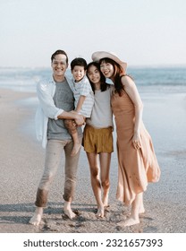 Asian Family Hugging and Walking Along the Beach with Father, Mother, Teenage Girl, Boy, during Sunset on the Shore with Ocean Background and Sunlight