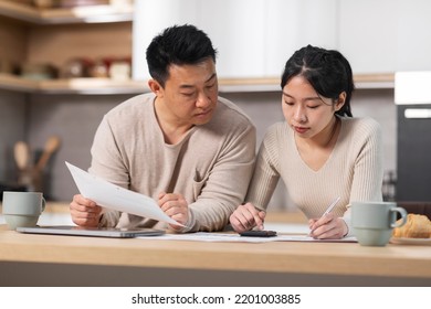 Asian Family Husband And Wife Sitting At Kitchen Table Full Of Papers, Laptop, Coffee Mugs, Counting Monthly Expenses, Using Calculator, Short Of Money, Spouses Working On Family Budget