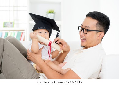 Asian family lifestyle at home. Baby with graduation cap holding certificate with father. Parent and child early education concept.