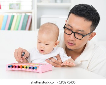 Asian family lifestyle at home. Father playing music instrument with baby. Sound development concept.