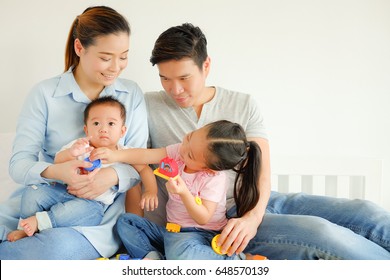 Asian Family And Little Cute Girl Playing Colorful Toys With Parents On Bed