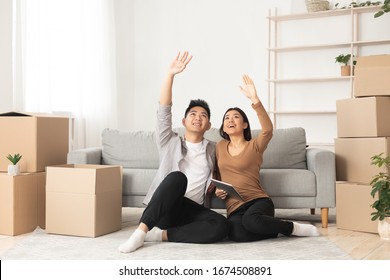 Asian Family Looking Up, Sitting On Floor In New Apartment With Moving Boxes, Dreaming About Future, Pointing Upward