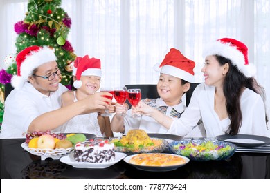 Asian Family Looks Happy While Toasting Glasses Of Syrup Before Having Christmas Dinner At Home