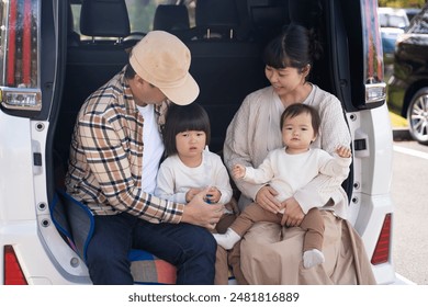 Asian family in the luggage compartment of a car playing in the autumn park - Powered by Shutterstock