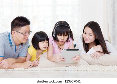 Asian Family Lying On Floor Using Tablet Computer