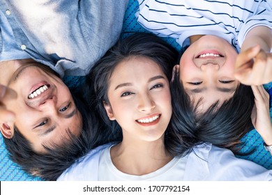 Asian Family Lying On Sheet Mat Smiling Face, Looking At Camera Showing Beautiful White Teeth. Mother Is In Middle Between Father And Kid. Strong White Healthy Teeth For Dental Care Clinic Concept.