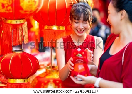 Asian family mother and daughter holding red shopping bag during choosing and buying home decorative ornaments and joss paper for celebrating Chinese Lunar New Year festival at Chinatown street market