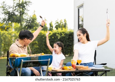 An Asian Family Of Parents And Daughters Camping With BBQ Tires. In The Front Yard Outside The House Together Happily