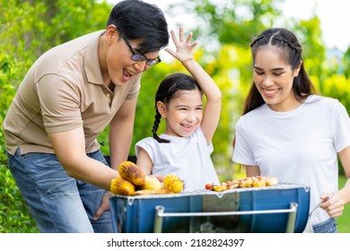 An Asian Family Of Parents And Daughters Camping With BBQ Tires. In The Front Yard Outside The House Together Happily