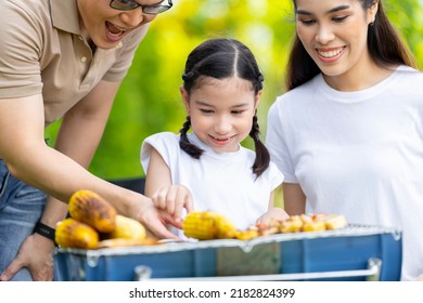 An Asian Family Of Parents And Daughters Camping With BBQ Tires. In The Front Yard Outside The House Together Happily