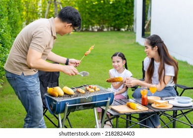 An Asian Family Of Parents And Daughters Camping With BBQ Tires. In The Front Yard Outside The House Together Happily