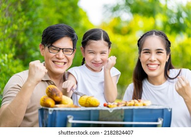 An Asian Family Of Parents And Daughters Camping With BBQ Tires. In The Front Yard Outside The House Together Happily