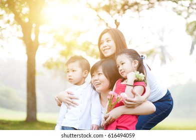 Asian Family At Park, Parents And Children, Outdoor In Morning With Sun Flare.