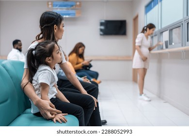 Asian family patient wait on line queue to receive medicine in hospital. Attractive mother and daughter sit on chairs, waiting the pharmacy counter to provides services to patients in medical center.