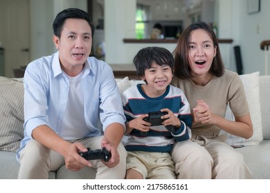 Asian Family Play Video Game With Joystick Togather In Living Room On Sofa. Father Mother And Son Playing Game Console Togather