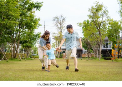 Asian Family Playing Catch On Yard Or Public Park In Neighborhood For Daily Health And Well Being, Both Physical And Mental Happy Family.