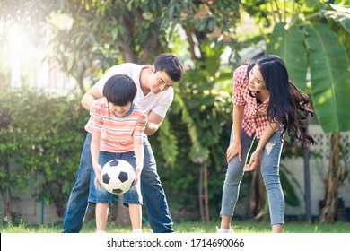 Asian Family Playing Football In Garden At Home Together. Father Teaching Son To Kick And Catch Ball On Green Grass While Mother Cheer Boy Up. Happy Lovely Family Enjoy Outdoor Activity In Backyard.