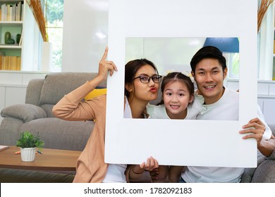 Asian Family Portrait Holding White Photo Frame And Smile Together. Thai People Enjoy Their Life In The Living Room.