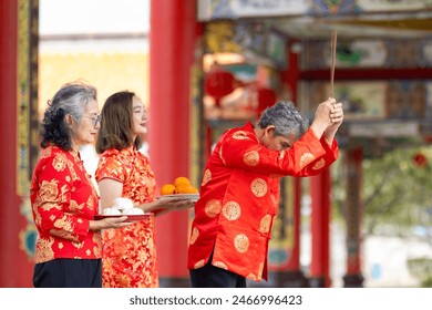 Asian family with senior parent in red cheongsam qipao dress is offering food to the ancestral god inside Chinese Buddhist temple during lunar new year for best wish blessing and good luck - Powered by Shutterstock