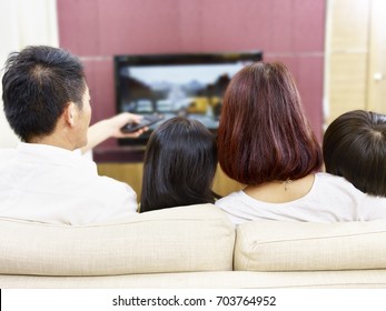 Asian Family Sitting On Couch At Home Watching TV, Rear View.
