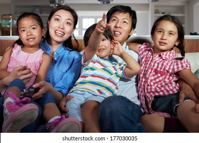 Asian Family Sitting On Sofa Watching TV Together