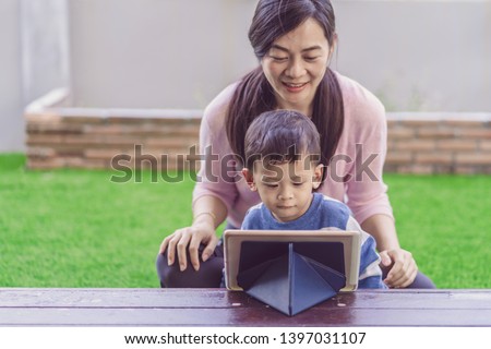 Asian family with son are looking the cartoon via technology tablet and playing together when living in front lawn for Self learning or home school,Family home school concept