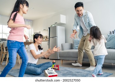 Asian Family Spending Time Together On Holiday In Living Room At Home. Attractive Happy Parents, Father Play With Young Little Two Kid Girl Daughter Run Around Mother In House. Activity Relationship.