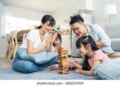 Asian family spending time together on holiday in living room at home. Attractive happy parents, father and mother play wood block toy with young two kid girl daughter in house. Activity relationship.