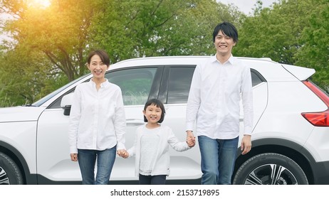 Asian Family Standing In Front Of A Car. Eco Car. Electric Vehicle.