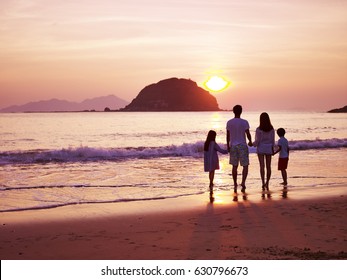 Asian Family Standing On Beach Watching And Enjoying The Sunrise.