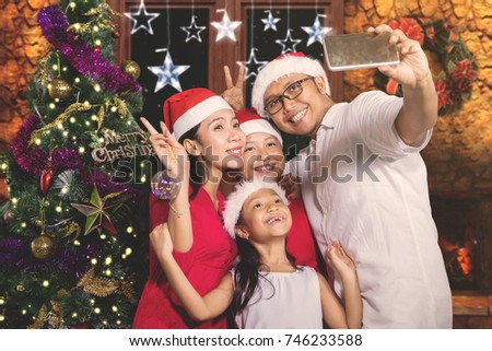 Asian family taking a selfie photo by using a smartphone while celebrating Christmas in the living room